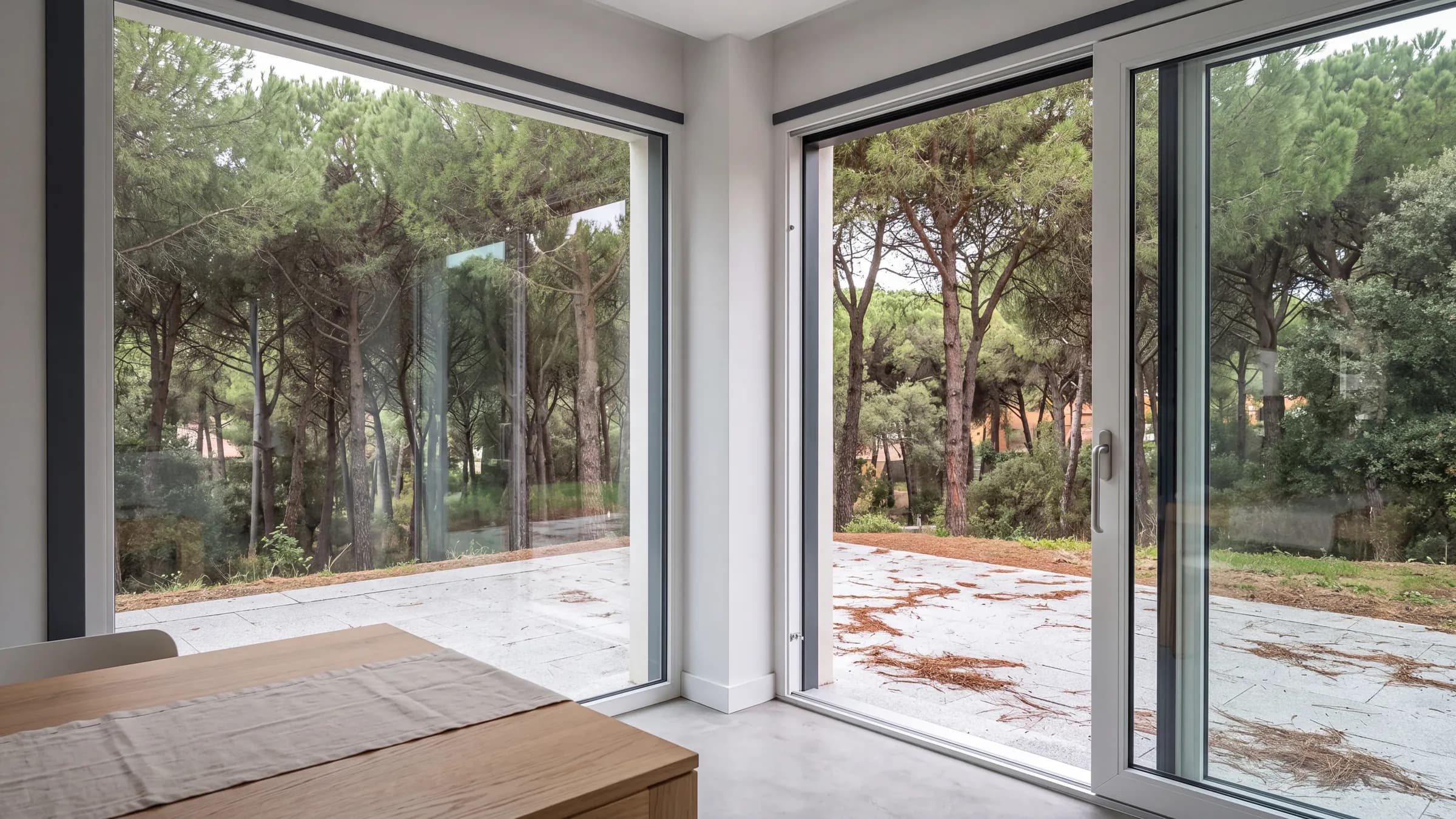 Chalet junto a un pinar con un ventanal en esquina: un fijo en una cara y una corredera elevable abierta en la otra