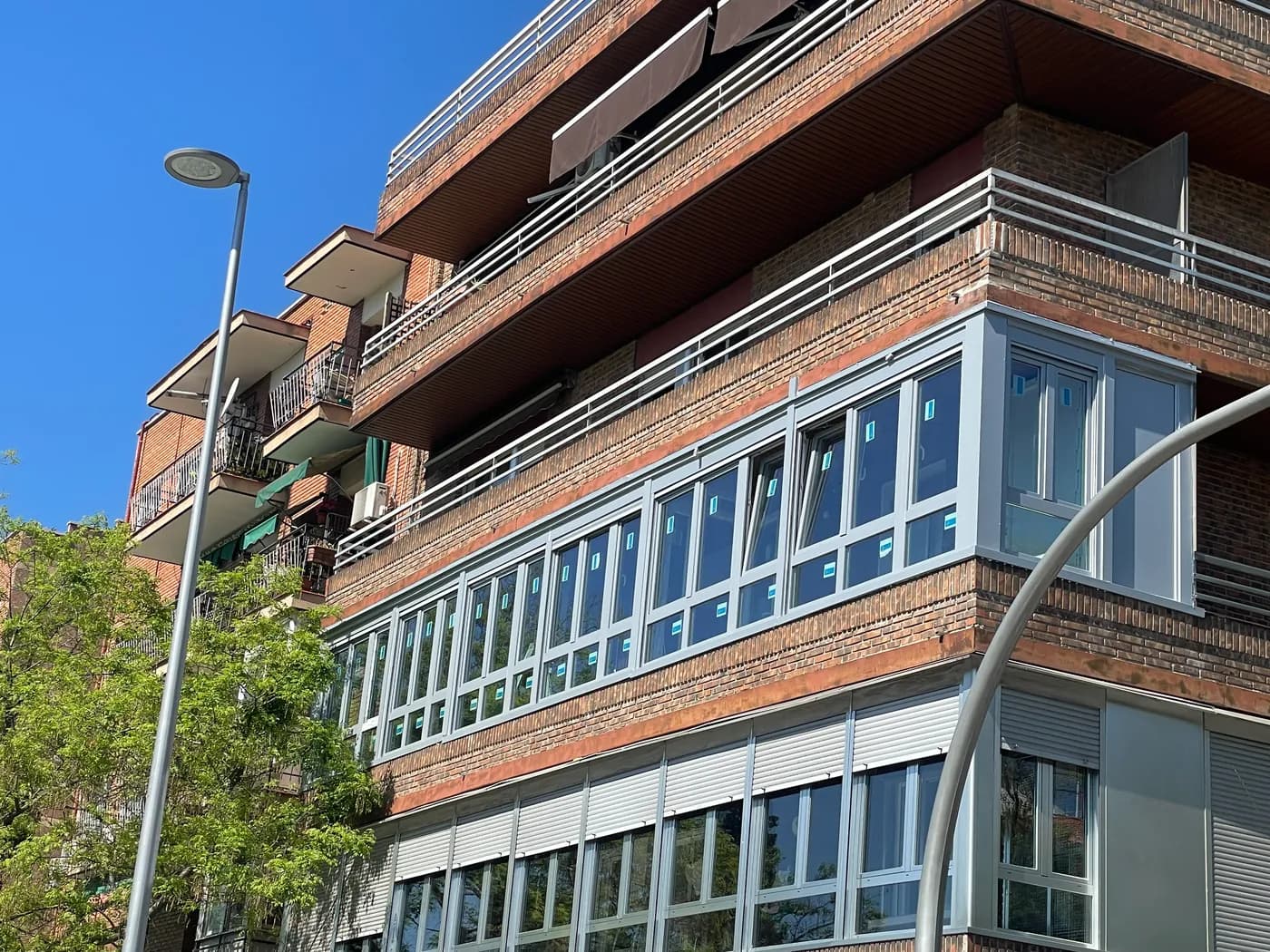 Edificio de ladrillo en esquina con una planta entera cerrada con carpintería gris recién instalada, con las etiquetas aún en los vidrios