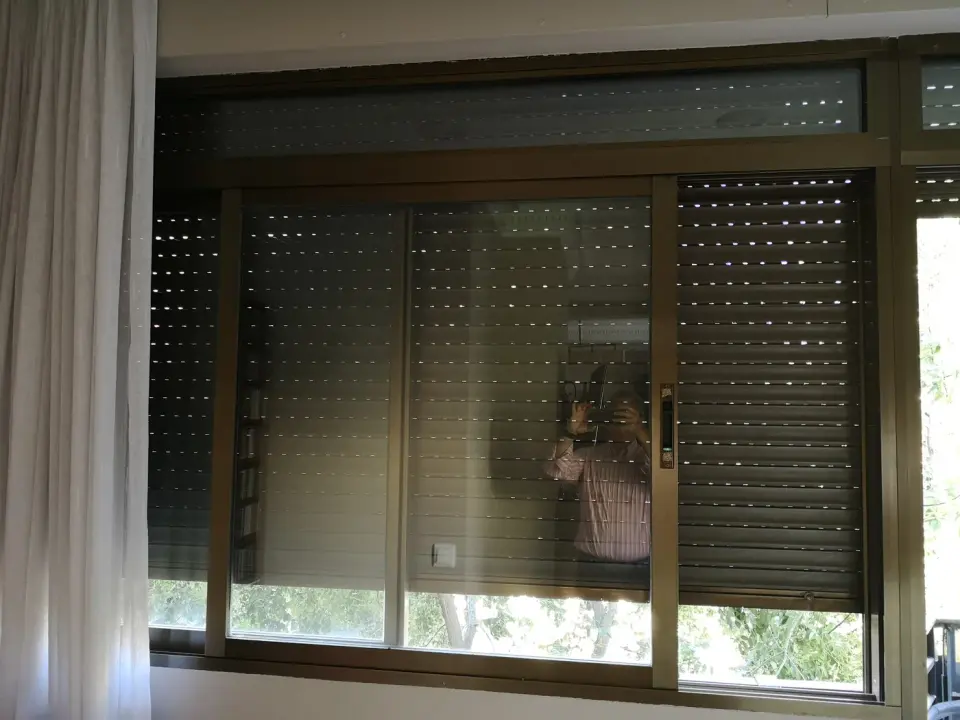 Ventana corredera antigua de aluminio de dos hojas con montante superior y la persiana bajada por fuera