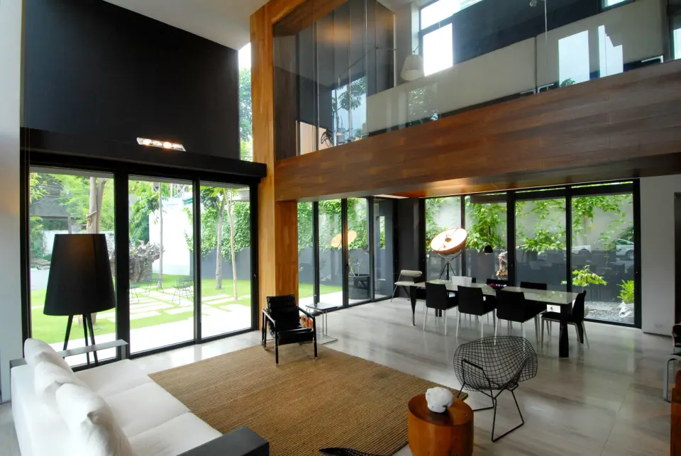 Salón de doble altura con grandes puertas correderas de perfil oscuro abiertas a un jardín