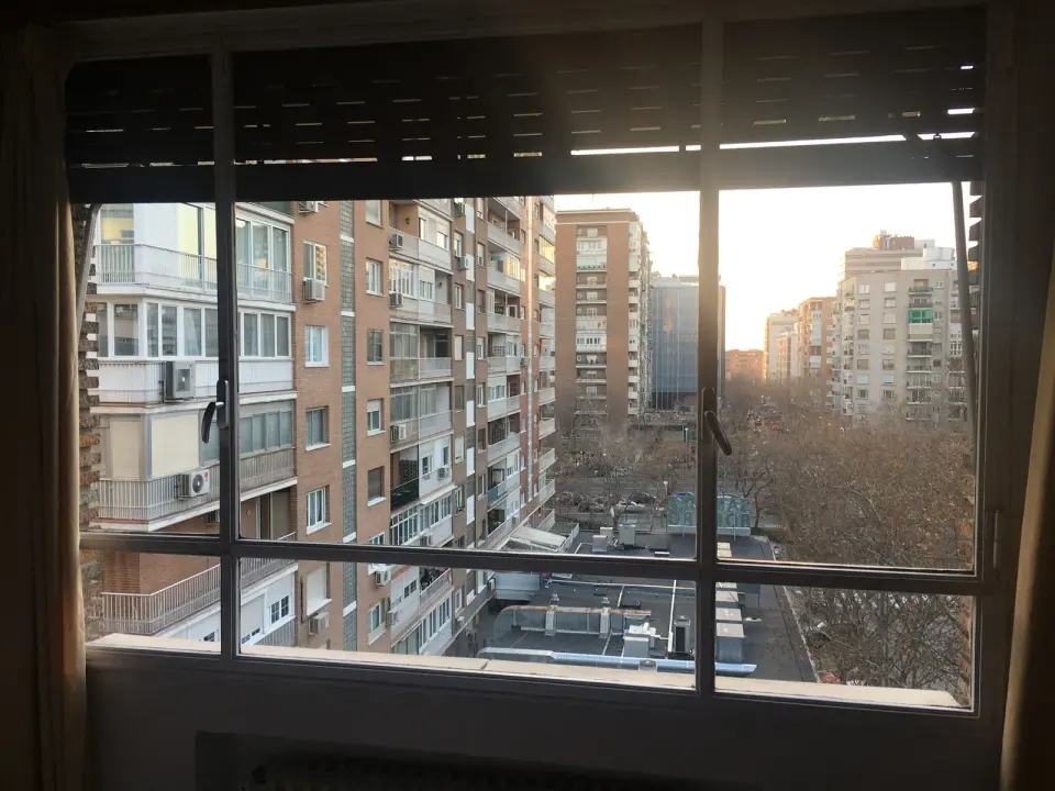 Ventana antigua de aluminio de varias hojas con la persiana a media altura y vistas a edificios de viviendas