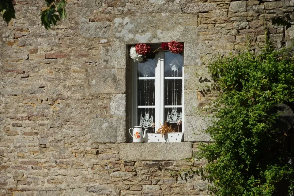 Ventana blanca en un muro de mampostería con un alféizar exterior de un solo bloque de granito que apenas sobresale de la pared