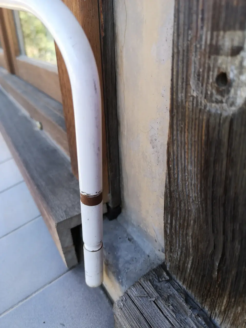 Marco de madera antiguo muy agrietado junto a una tubería blanca en una fachada