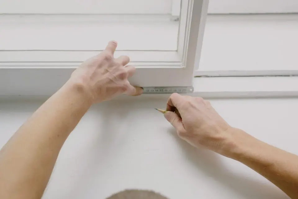 Manos midiendo con un metro el marco blanco de una ventana abierta