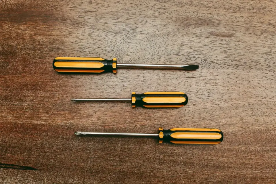 Tres destornilladores de mango amarillo y negro sobre una mesa de madera