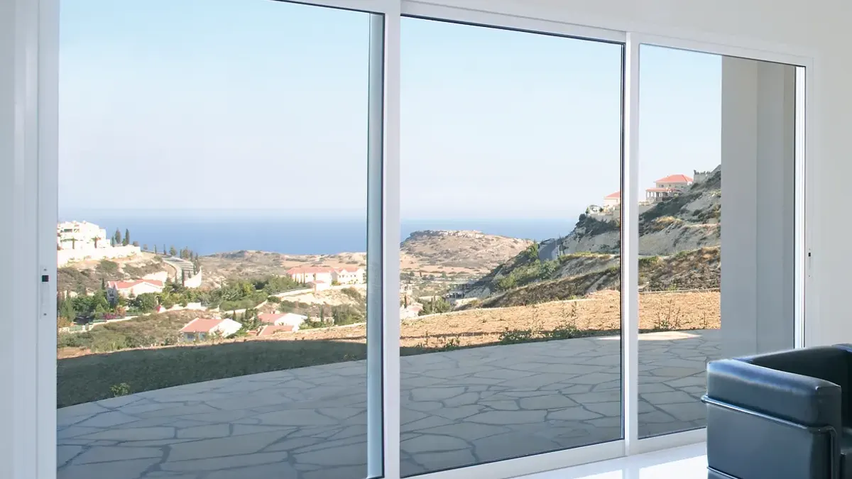 Gran corredera blanca de suelo a techo que se abre a una terraza con vistas al mar y a una ladera con casas