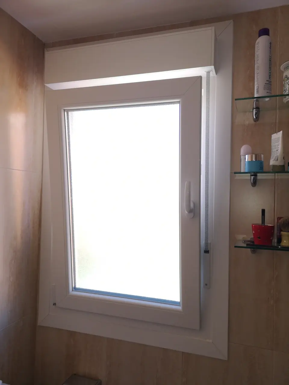 Ventana de PVC blanca de una hoja con vidrio translúcido y cajón de persiana en un baño de azulejo beige