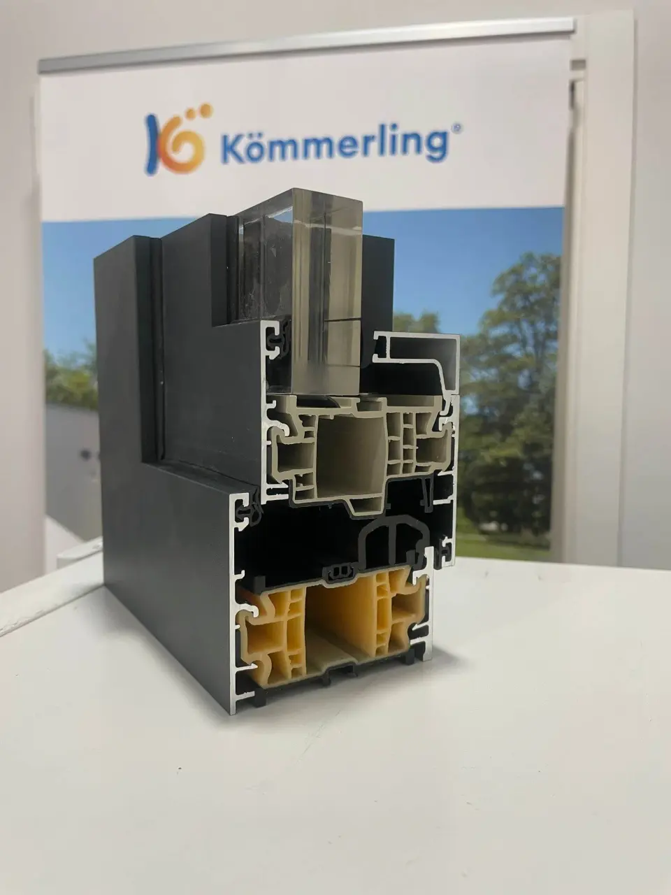 Corte de un perfil de ventana Kömmerling AluNext con su vidrio montado, sobre un expositor