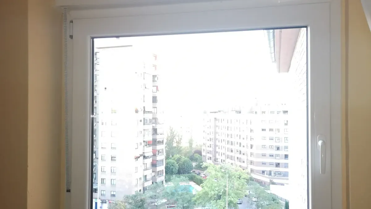 Ventana de PVC blanca oscilobatiente con cajón de persiana en un piso, con vistas a bloques de viviendas