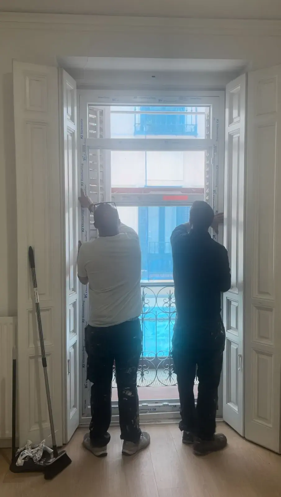 Dos operarios de espaldas colocando una balconera de PVC blanca en un edificio antiguo