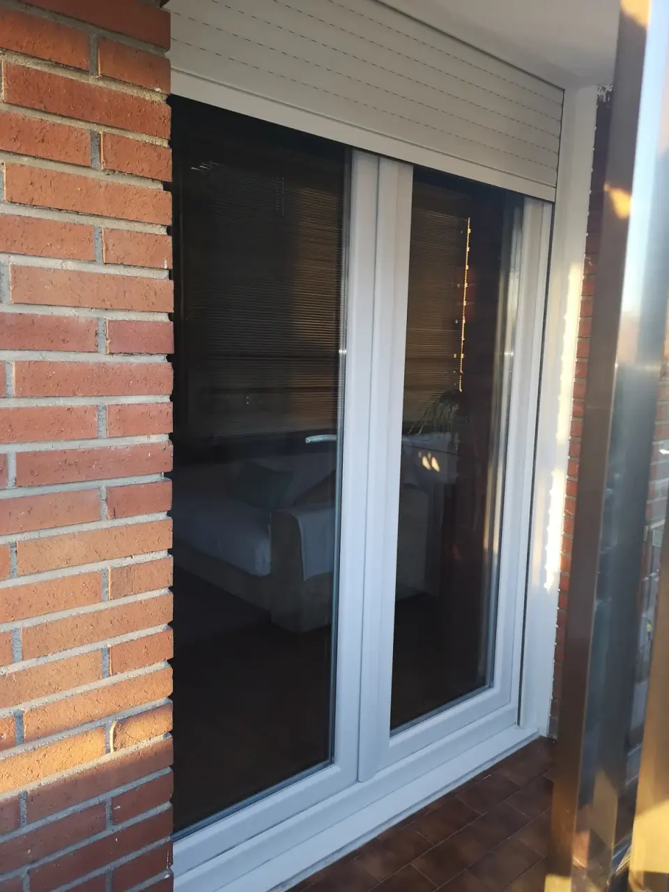 Balconera de PVC blanca de dos hojas vista desde la terraza, con la persiana de lamas claras algo bajada