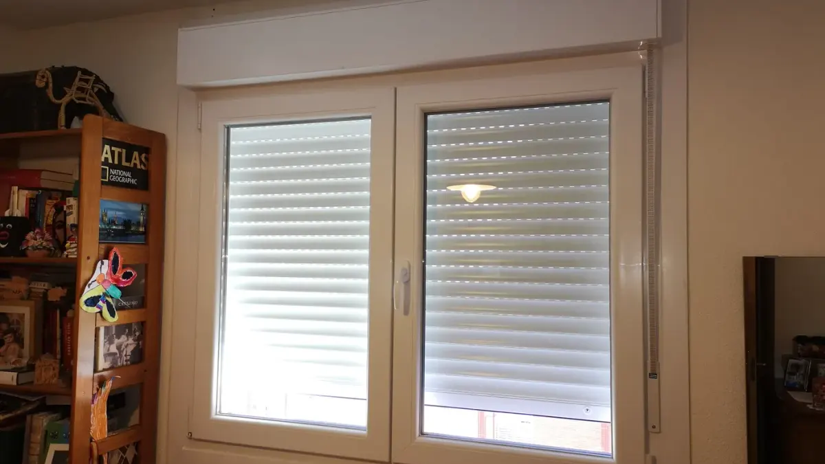 Ventana de PVC blanca de dos hojas con cajón de persiana, la persiana a media altura y la cinta a la derecha