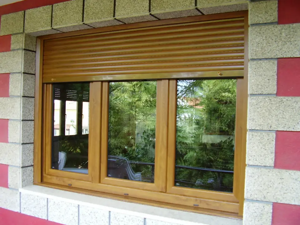 Ventana de PVC imitación madera de tres hojas con la persiana enrollable del mismo acabado bajada en parte