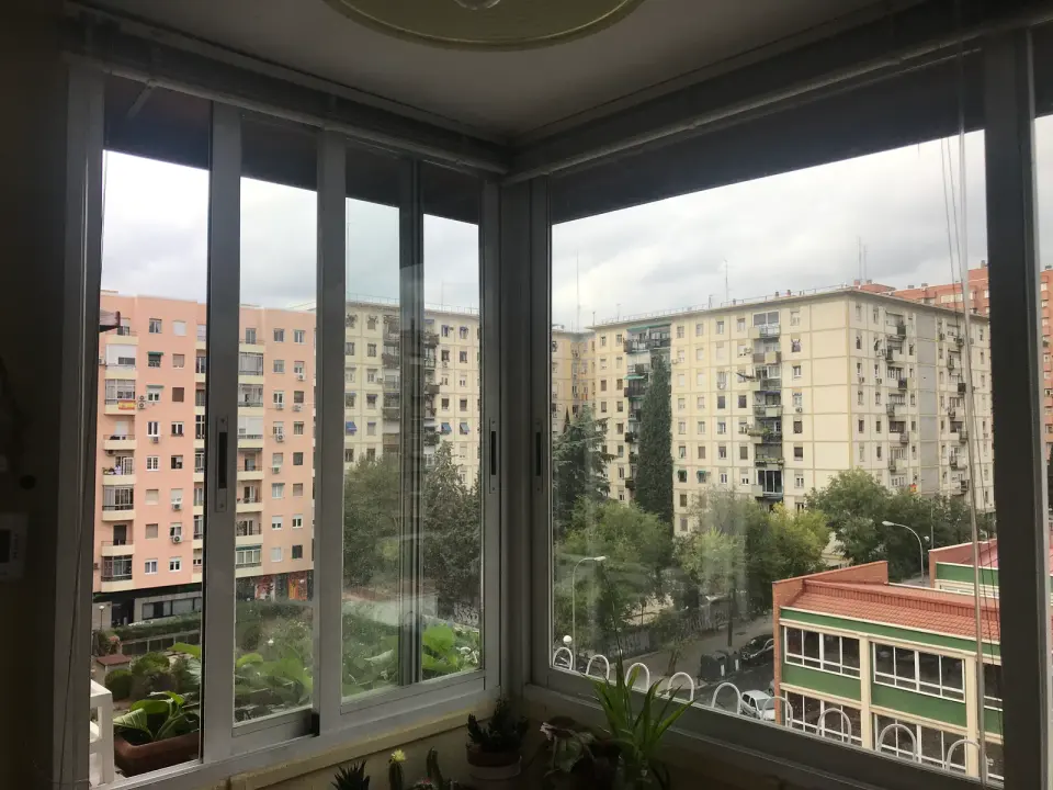 Ventanas correderas antiguas de aluminio en una galería en esquina, con varias hojas y vistas a bloques de viviendas