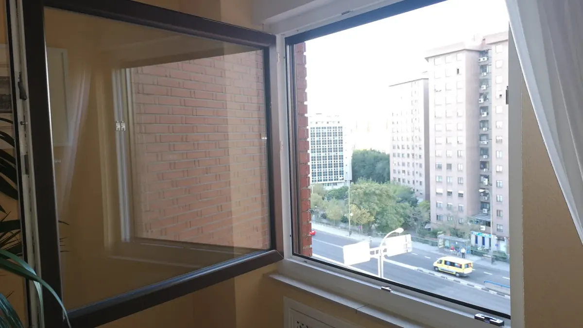 Ventana de PVC blanca de una hoja abierta hacia dentro, con la cara exterior de la hoja en color oscuro