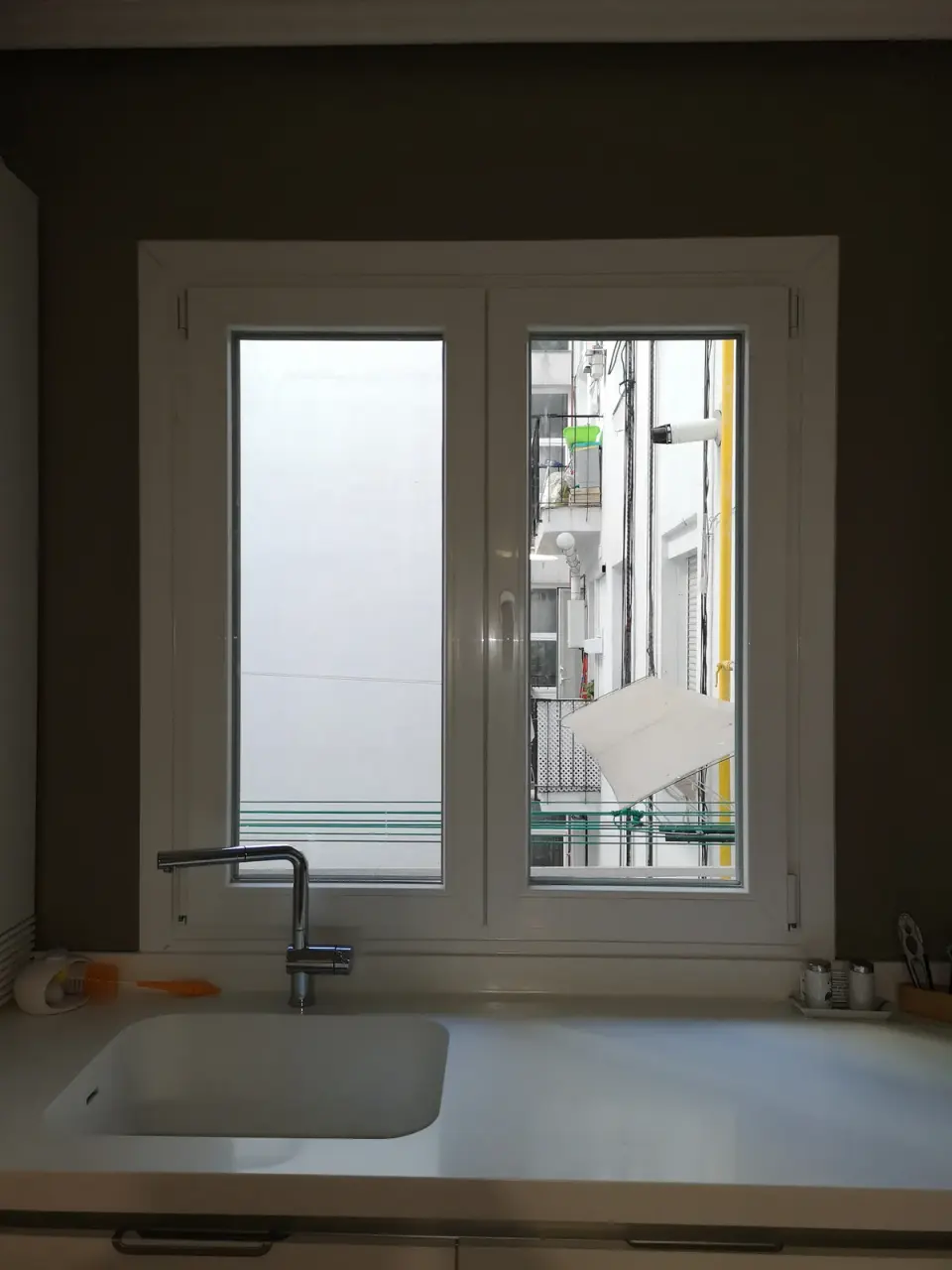Ventana de PVC blanca de dos hojas sobre la encimera de una cocina, con el grifo del fregadero delante