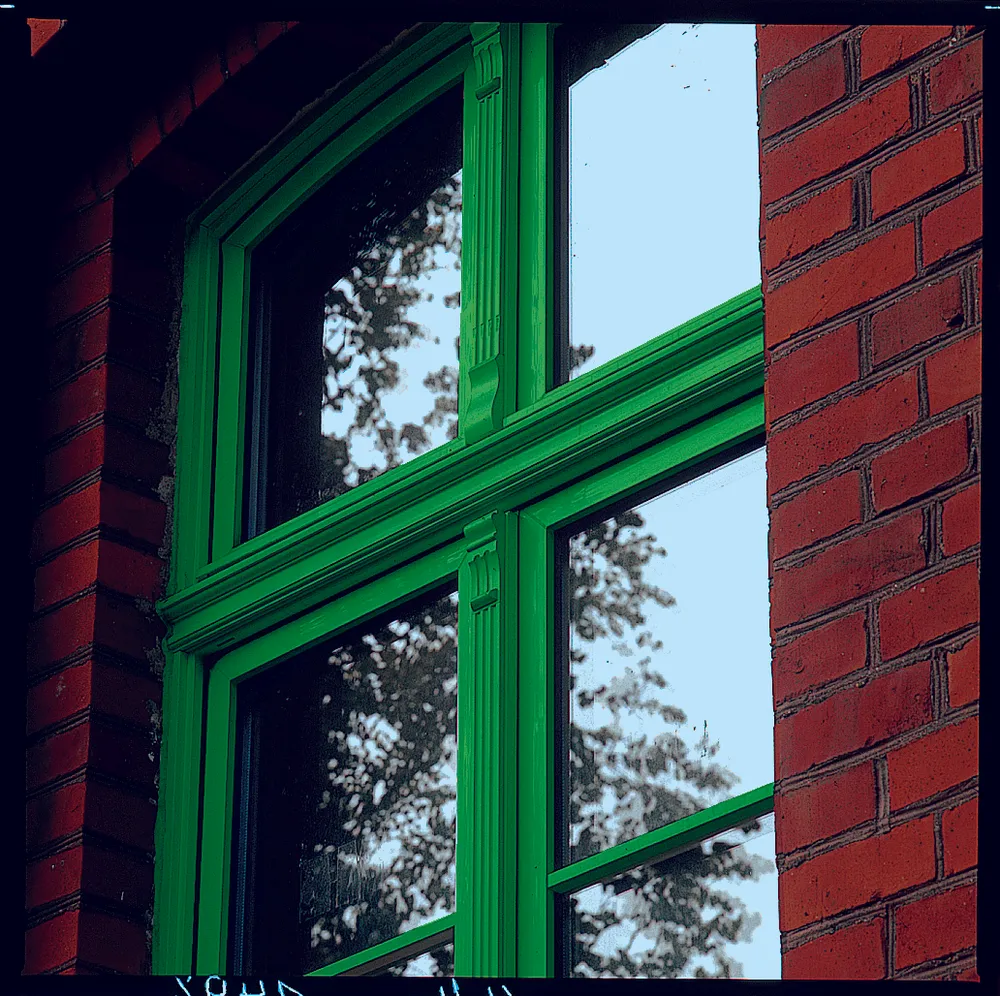 Ventana de PVC verde de varias hojas en una fachada de ladrillo