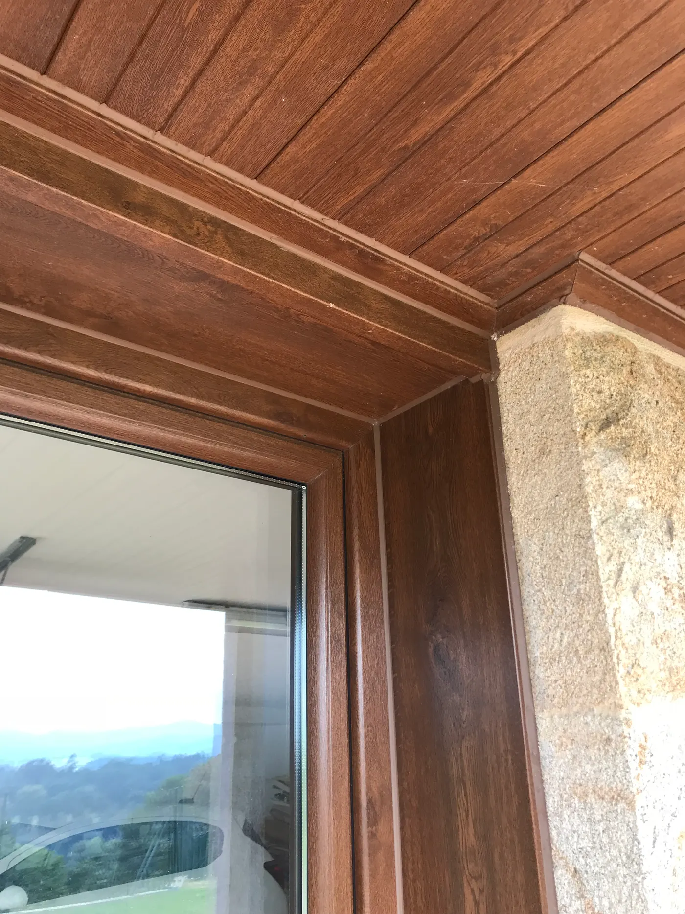 Detalle del marco de una ventana de PVC foliada en imitación madera junto a un techo de madera