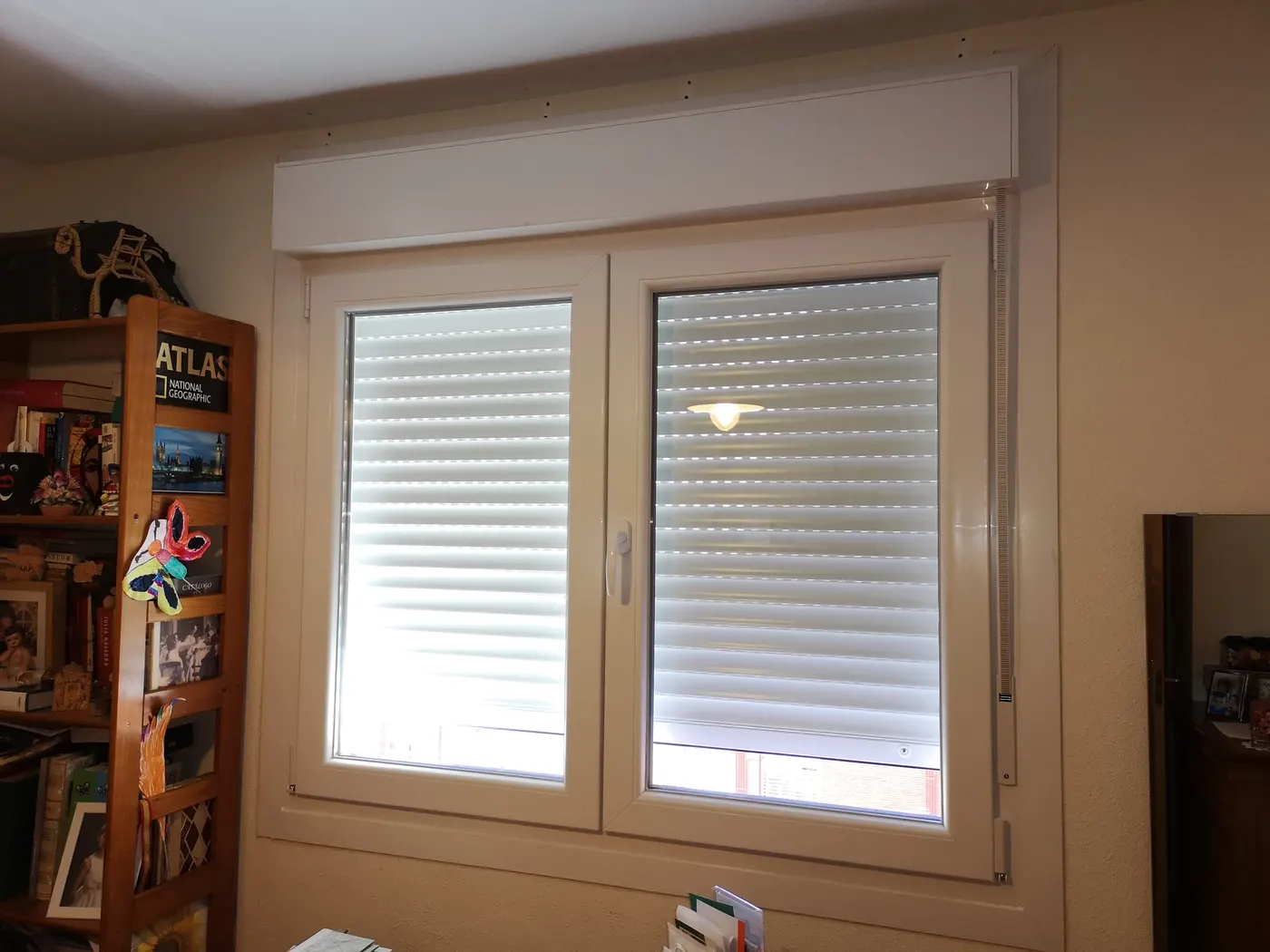 Ventana de PVC de dos hojas con cajón y persiana en un dormitorio.