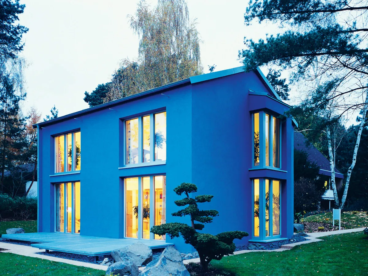 Casa azul de dos plantas con grandes ventanales iluminados al anochecer